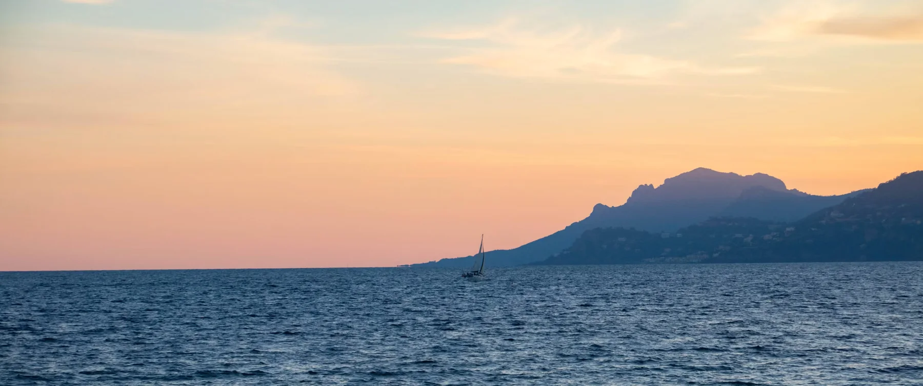 A sailboat at sunset in front of the Esterel mountains