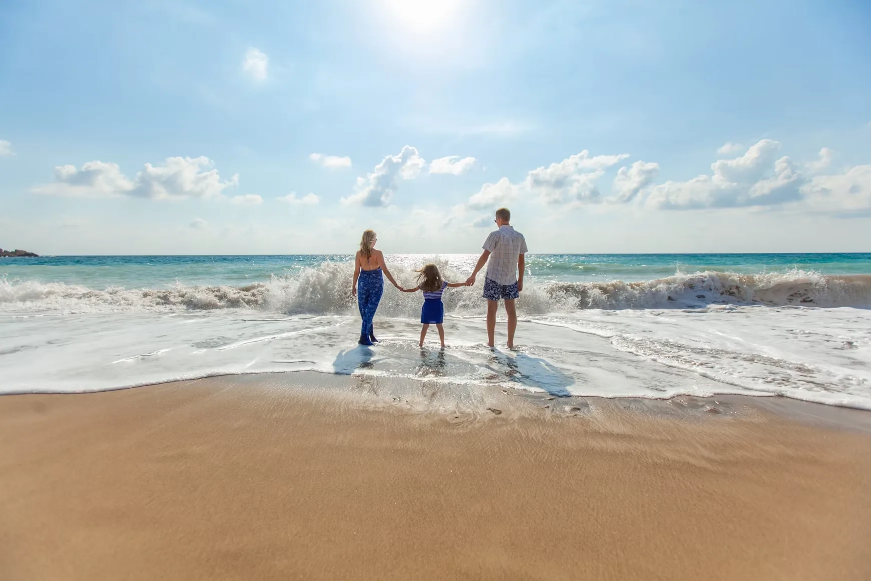A family holding hands in the waves on a sunny beach