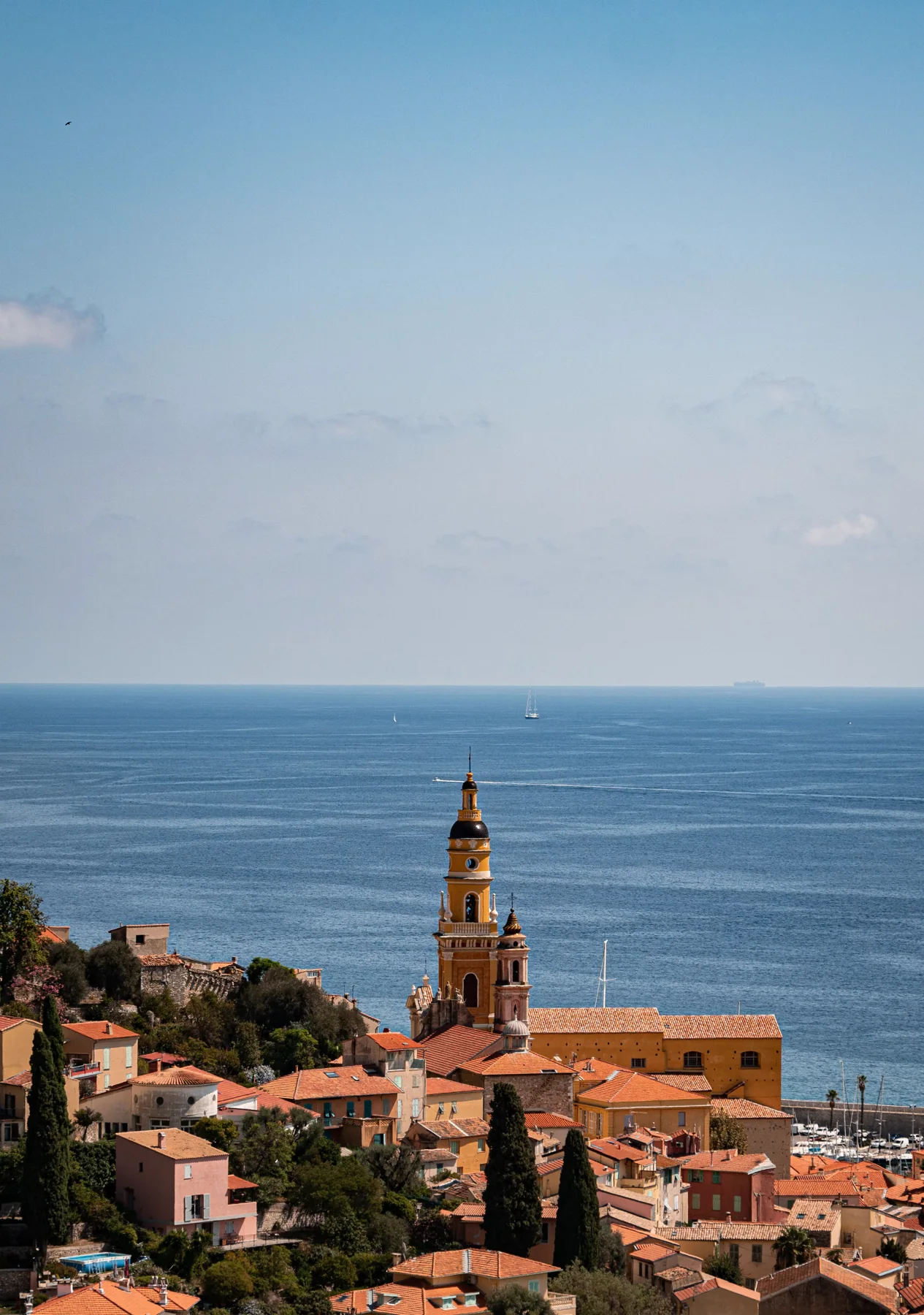 The bell tower of Menton's basilica above orange rooftops and the blue Mediterranean